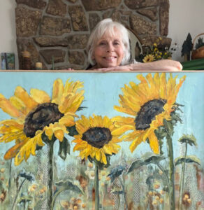 Saundra Lane standing behind her most recent painting of sunflowers basking in the sun.